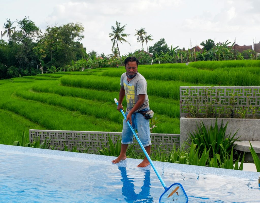man in white polo shirt and blue denim jeans standing on swimming pool during daytime